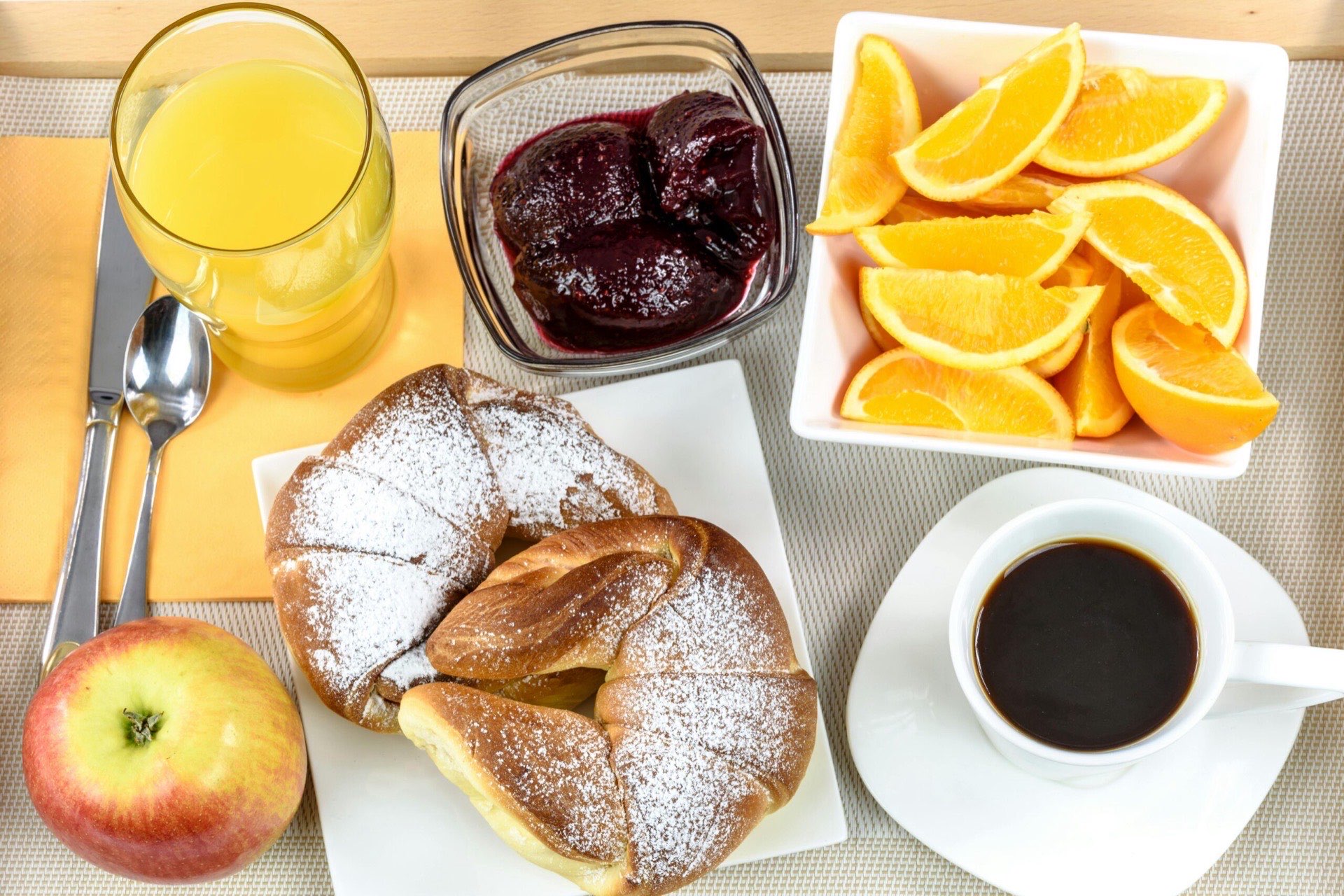 Frühstück von oben: Croissants, Orangensaft, Kaffee, Marmelade, Orangenspalten und ein Apfel
